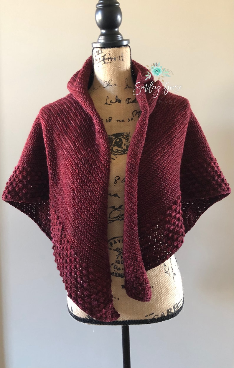 May include: A maroon crocheted shawl with a hood and a textured border. The shawl is draped over a mannequin.