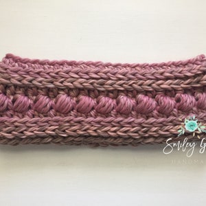 Puede incluir: Una diadema de crochet rosa con un dise&ntilde;o texturizado. La diadema tiene una fila de peque&ntilde;os bultos en relieve.