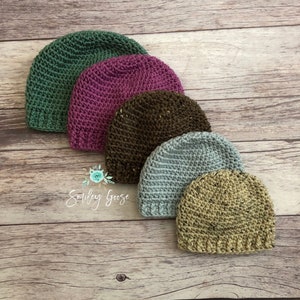 May include: Five crocheted hats in different colors and textures. The hats are arranged in a row from largest to smallest. The colors are green, purple, brown, blue, and beige.