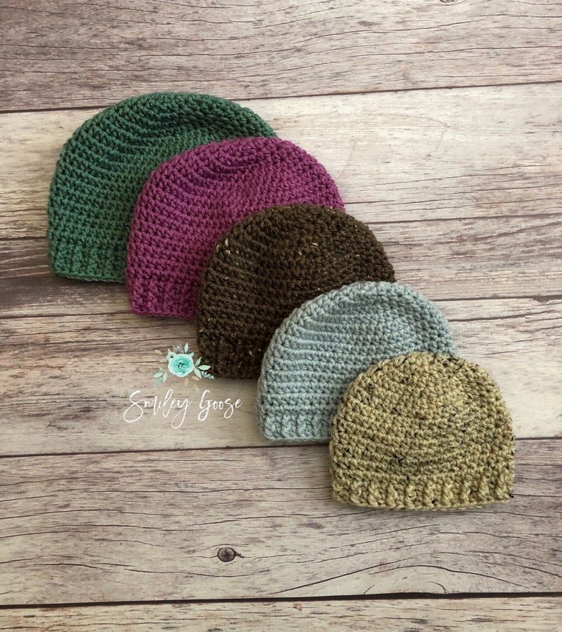 May include: Five crocheted hats in different colors and textures. The hats are arranged in a row from largest to smallest. The colors are green, purple, brown, blue, and beige.