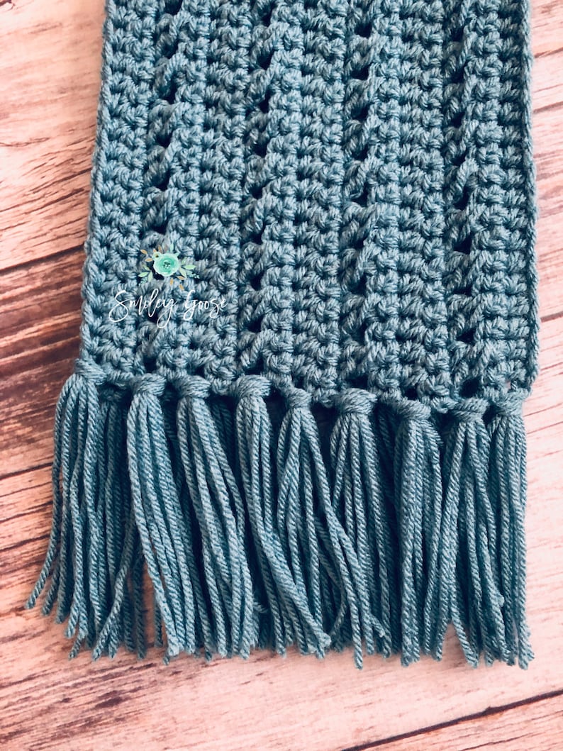 May include: A teal blue crocheted scarf with a fringe on the bottom edge.