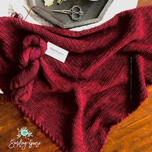 May include: A burgundy crocheted shawl with a label that reads "Hawthorne" and a tag that reads "Smiley Goose Handmade".