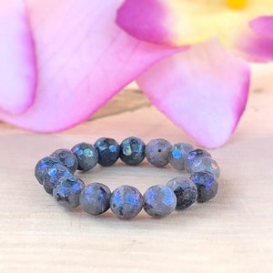 May include: A dark blue labradorite gemstone bracelet with a round shape. The bracelet is made of small, faceted beads.