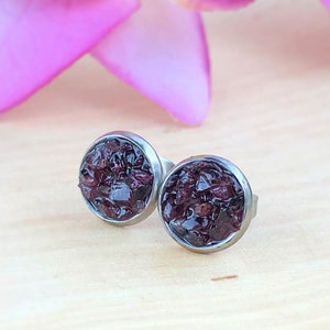 May include: A pair of silver stud earrings with a round, dark purple, glittery design.