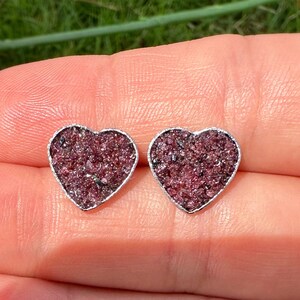 May include: A pair of heart-shaped earrings with a silver setting and a pink, sparkly, crushed stone filling.