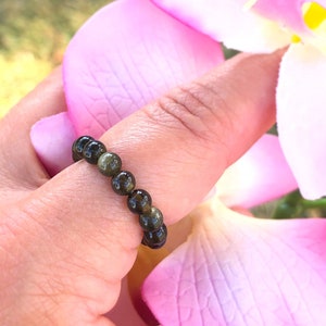 May include: A green and black beaded ring worn on a finger. The ring is made of small, round beads that are strung together.