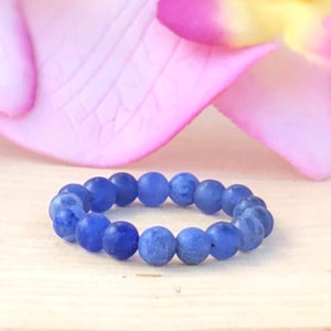 May include: A blue gemstone beaded ring on a wooden surface. The ring is made of small, round beads that are strung together to form a circle.