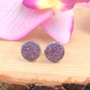 Puede incluir: Un par de pequeños pendientes de botón redondos con un engaste plateado y un centro morado claro brillante.