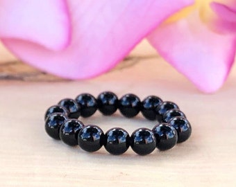 Peut inclure: Un bracelet noir en perles rondes en onyx poli. Le bracelet est posé sur une surface en bois brun clair.