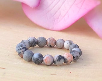 Peut inclure: Un bracelet en perles grises, roses et noires avec un élastique.