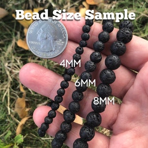 May include: Three strands of black lava rock beads in different sizes, 4mm, 6mm, and 8mm, are laid out on a hand for size comparison. A US quarter is included for scale.