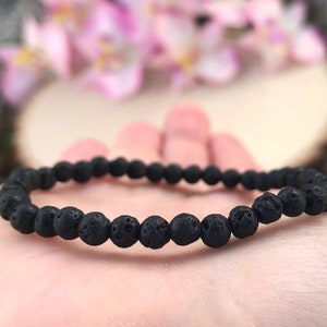 May include: A black lava rock beaded bracelet. The bracelet is made of small, round beads that are strung together on a thin elastic cord.