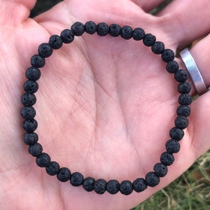 May include: A black lava rock beaded bracelet. The bracelet is made of small, round beads with a rough, textured surface.