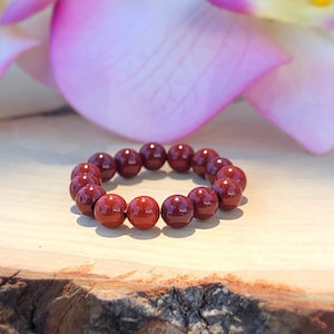 May include: A red gemstone bracelet with round beads. The bracelet is on a wooden surface.