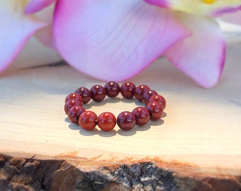 Könnte beinhalten: Ein rotes Edelstein-Armband mit runden Perlen. Das Armband liegt auf einer Holzoberfläche.