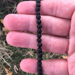 May include: A black lava rock beaded bracelet. The bracelet is made of small, round beads that are strung together on a black cord.
