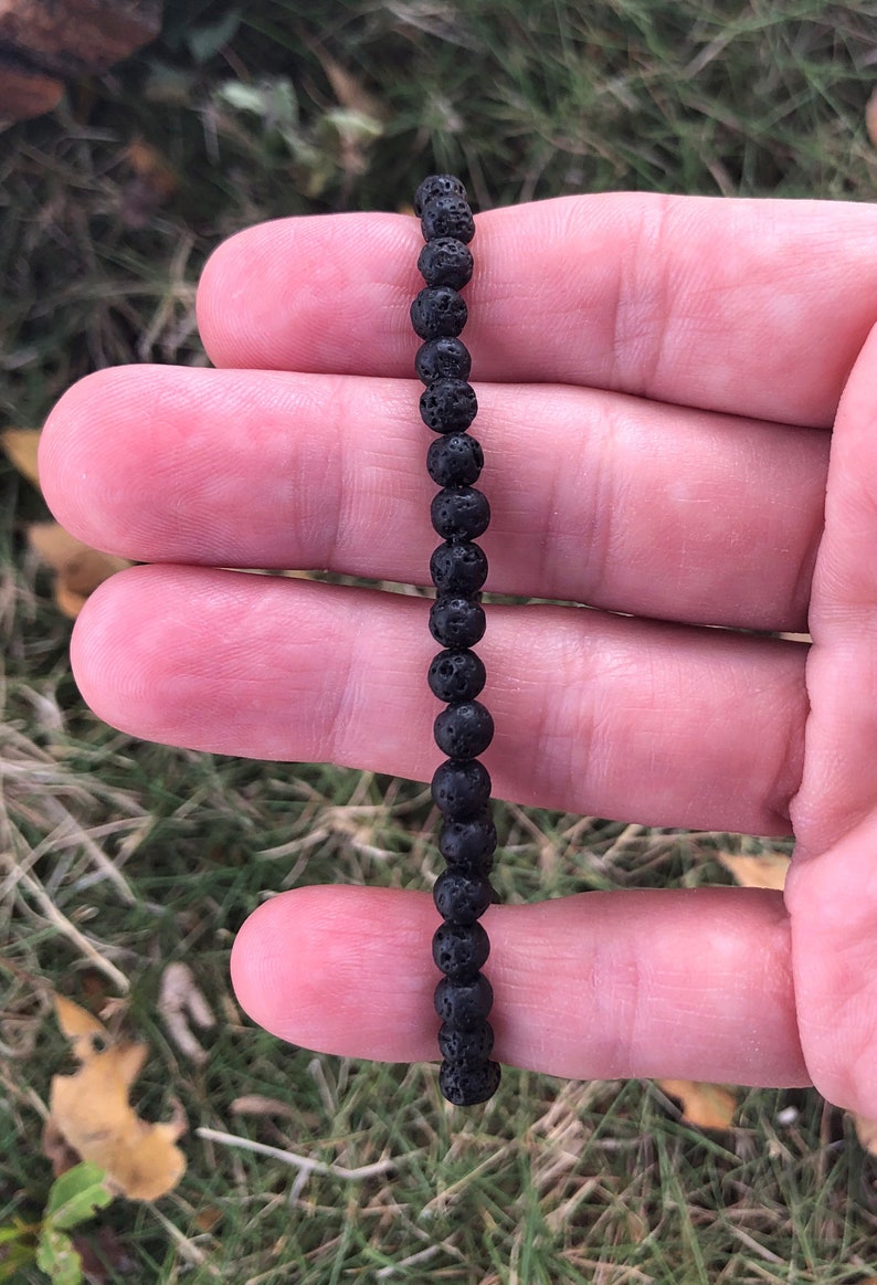 May include: A black lava rock beaded bracelet. The bracelet is made of small, round beads that are strung together on a black cord.