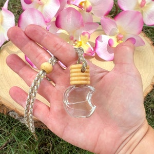 May include: A clear glass car air freshener with a wooden top and a gold string. The air freshener is shaped like a crescent moon and is hanging from a string.