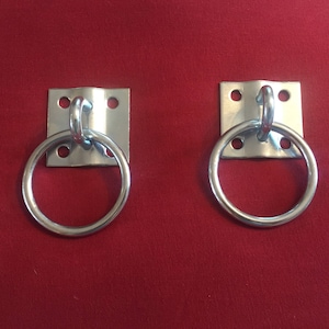 May include: Two silver metal rings with a square metal plate attached to the back. The rings are attached to the plates with a hook.