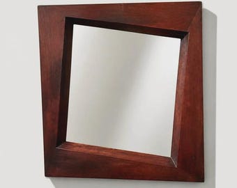 May include: A square wall mirror featuring a dark brown wooden frame with an asymmetrical, slanted design. The frame has wide, flat edges that taper towards the reflective glass centre, creating a geometric shape with non-parallel sides.