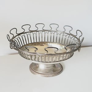 Peut inclure: Coupe à fruits en métal argenté avec un socle. Le bol présente un design ajouré avec des barres verticales et un bord festonné. L'intérieur est de couleur argent brillant. Un objet classique pour servir des fruits ou exposer des objets décoratifs, environ 25 cm de diamètre.