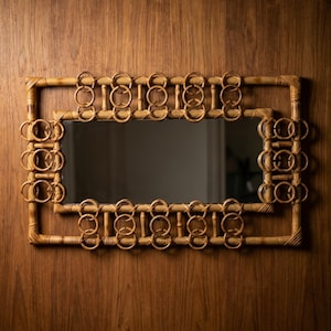 May include: Rectangular mirror with a woven bamboo frame. The frame has a double-layered design with decorative ring accents. The mirror is mounted on a wooden surface, creating a natural and textured aesthetic.