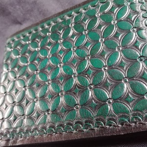 May include: A green leather wallet with a decorative embossed pattern of overlapping circles. The wallet has a black stitched border.