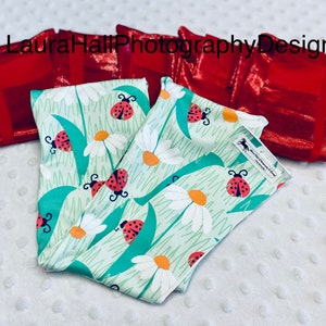 May include: A set of four red fabric headbands with a green and white headband with a ladybug and daisy print. The headband with the print has the text "Laura Hall Photography Design" on it.