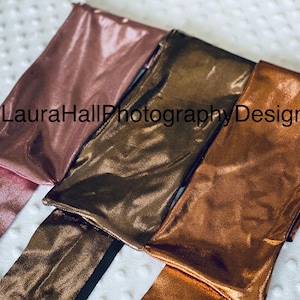May include: Three metallic fabric strips in rose gold, bronze, and copper colors. The fabric has a shimmery finish. The strips are arranged in a stack, with the rose gold strip on top.