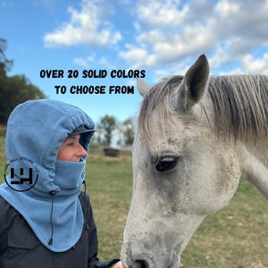 May include: A person wearing a light blue hood with a black jacket, interacting with a gray horse. The hood has a built-in visor and covers the neck and face. Text on the image reads "OVER 20 SOLID COLORS TO CHOOSE FROM".