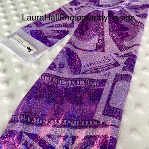 May include: Purple and white iridescent fabric with a dollar bill print. The fabric is glittery and has a subtle sheen.