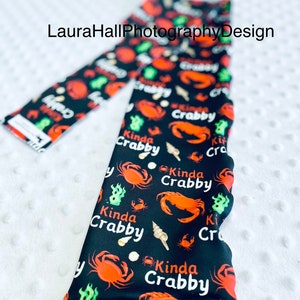 Op de afbeelding: Zwarte leggings met een herhalend patroon van rode krabben en de tekst "Kinda Crabby".