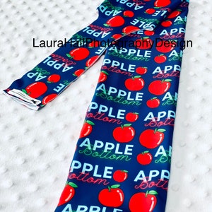 May include: A blue fabric leg warmer with a repeating pattern of red apples and the text "APPLE Bottom".