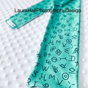 May include: A turquoise blue fabric headband with a repeating pattern of black letters and symbols. The text "Laura Hall PhotographyDesign" is visible on the headband.