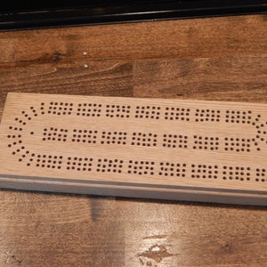 Op de afbeelding: Een houten spelbord met een raster van gaten, perfect voor een klassiek spelletje cribbage.