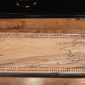 Op de afbeelding: Een houten cribbage-bord met een natuurlijke houten afwerking en een rand van gaten rond de randen.