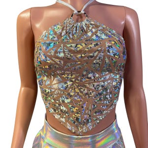 May include: Halter top with a geometric pattern. The top features a silver and iridescent design over a nude mesh base. It has a halter neck with a silver ring detail and a triangular shape.