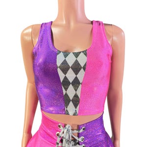 Könnte beinhalten: Ein zweiteiliges Outfit mit einem glitzernden, farbblockartigen Design. Das Oberteil ist ein Tanktop, vertikal geteilt in Lila und Pink. Ein Rautenmuster in Schwarz, Silber und Weiß akzentuiert die Mitte. Der Unterteil ist ein passender Rock mit Schnürdetail.