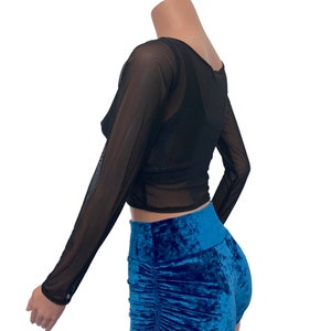 K&ouml;nnte beinhalten: Schwarzes, durchsichtiges, lang&auml;rmliges Crop-Top mit Rundhalsausschnitt. Das Top wird &uuml;ber einer blauen Samthose getragen.