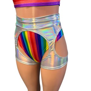 May include: High-waisted shorts featuring a metallic silver holographic finish with large circular cutouts on the sides. The shorts reveal a vibrant rainbow-striped fabric underneath, which also appears as a matching band at the top waistline.