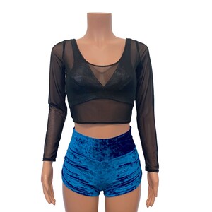 K&ouml;nnte beinhalten: Ein schwarzes, durchsichtiges Crop-Top mit langen &Auml;rmeln, Rundhalsausschnitt und blauen Samt-Shorts.