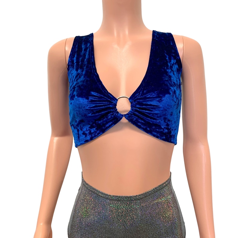 May include: A royal blue velvet crop top with a deep V-neckline and a gold-colored ring detail at the center. The top is sleeveless and has a soft, textured appearance, suitable for a night out or festival wear.