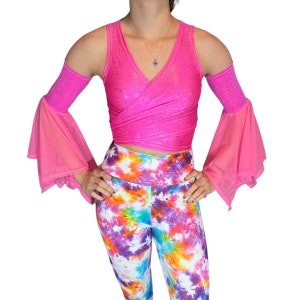 May include: A pink wrap crop top with a sparkly finish and sheer pink bell sleeves. The top is worn over a pair of colorful tie-dye leggings.