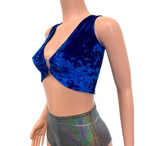 May include: A royal blue velvet crop top with a plunging neckline and a silver ring detail. The sleeveless top is paired with high-waisted, iridescent shorts. The fabric has a crushed velvet texture.