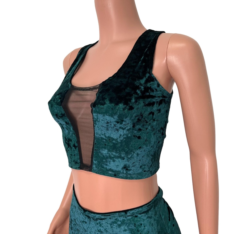 May include: A green velvet crop top with a black mesh panel in the front. The top has a scoop neckline and thin straps.