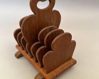 May include: A brown wooden letter holder featuring a series of five vertical dividers with rounded, scalloped edges. The tallest central divider includes a cutout handle at the top, and the entire structure is supported by a rectangular base with feet.