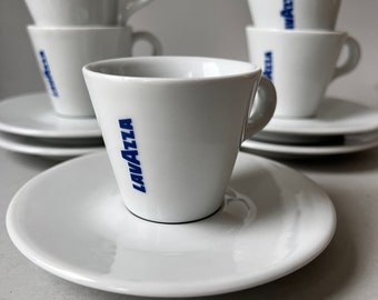 May include: A set of white espresso cups and saucers with the blue "Lavazza" logo. The cups are stacked on top of each other and the saucers are placed underneath.