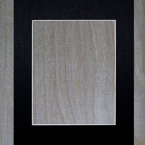 May include: A black picture frame with a white mat. The frame is on a light wood background.