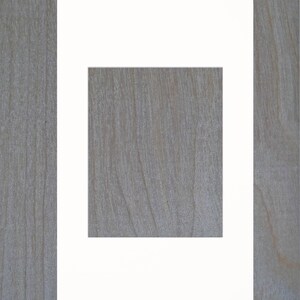 May include: A white mat with a square opening in the center. The mat is on a woodgrain background.