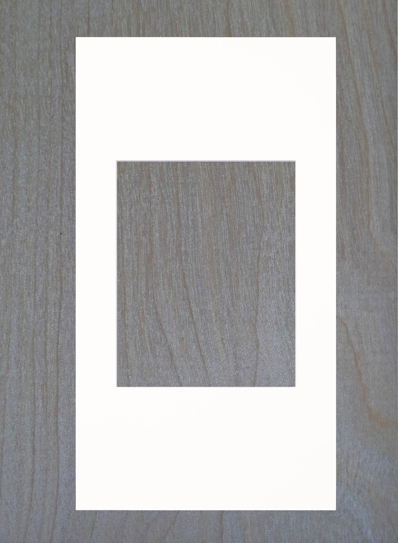 May include: A white mat with a square opening in the center. The mat is on a woodgrain background.